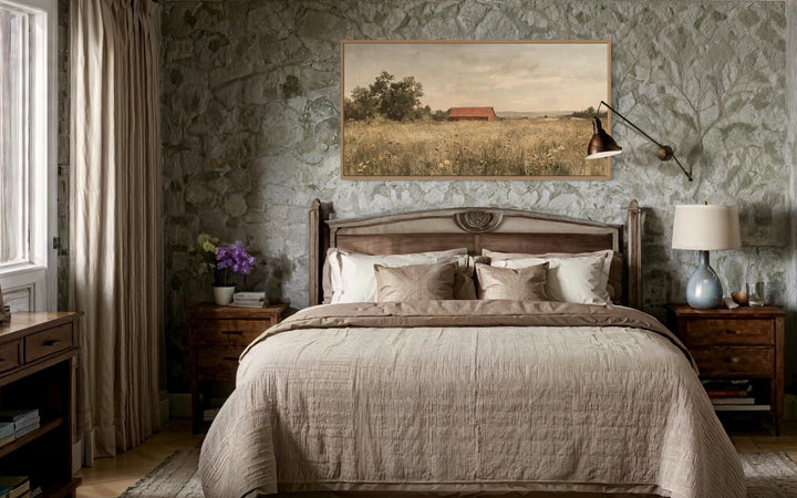 Red barn in a wildflower field landscape wall art hanging above a bed in a rustic stone bedroom.