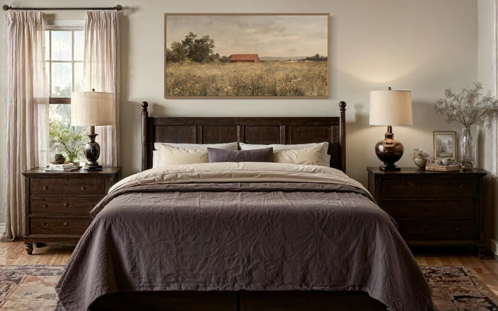 Red barn in a wildflower field landscape wall art hanging above a dark wood bed in a farmhouse room.