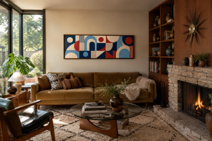 Long narrow Bauhaus canvas print with red and blue geometric shapes above a mid-century modern sofa.