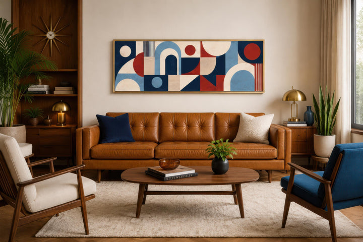 Long narrow Bauhaus wall art with red, navy, and cream geometric shapes above a tan leather sofa.