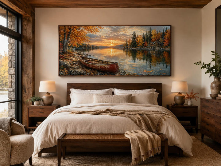 Red canoe on an autumn lake shore with a rustic cabin and forest canvas wall art above a bed.