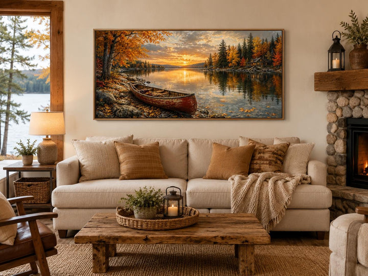 Red canoe on an autumn lake shore canvas wall art hanging above a beige sofa in a rustic living room.