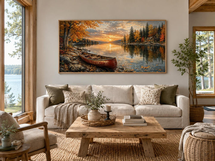 Red canoe on an autumn lake shore canvas wall art hanging above a sofa in a rustic living room.