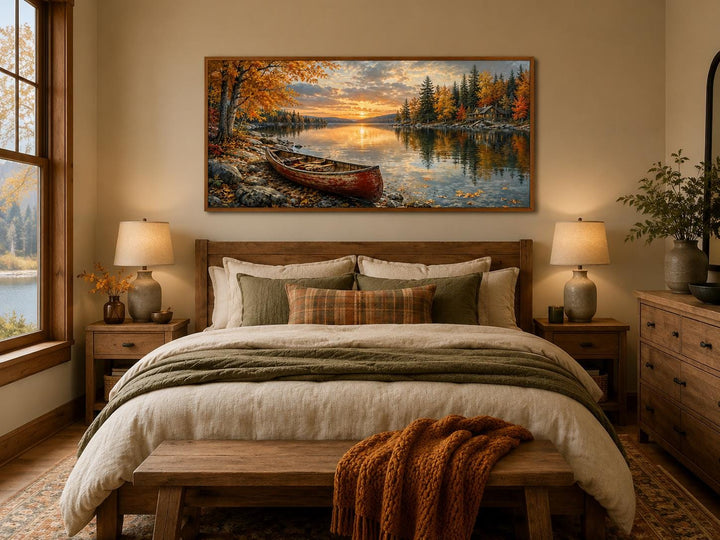 Red canoe on an autumn lake shore canvas wall art hanging above a bed in a rustic bedroom.