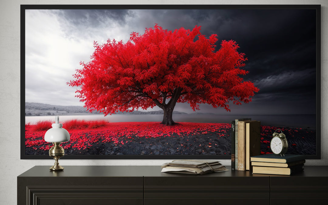 Framed canvas print of a vibrant red tree against a monochrome landscape on a black console table.