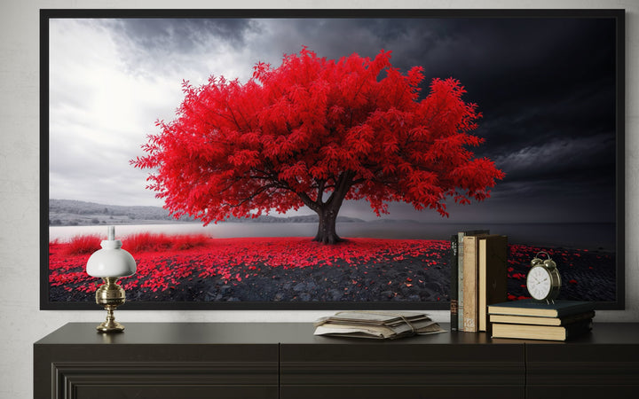 Framed canvas print of a vibrant red tree against a monochrome landscape on a black console table.