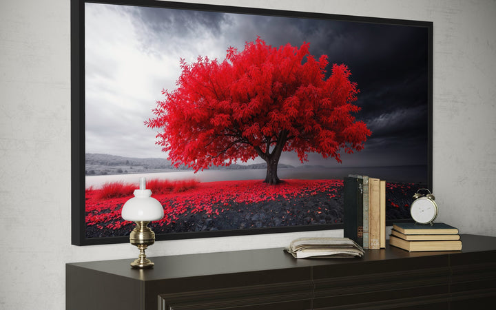 Framed canvas print of a vibrant red tree against a monochrome landscape on a dark wood console.