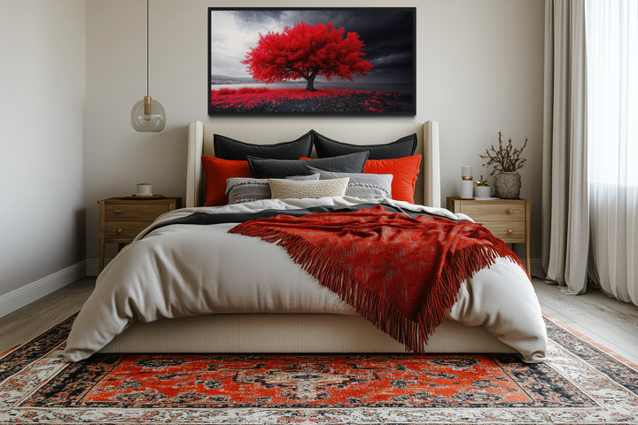 Framed canvas print of a vibrant red tree against a black and white landscape above a bed.