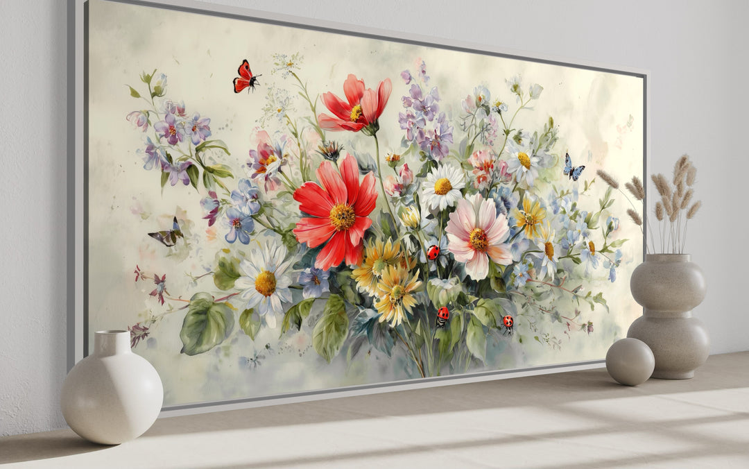 Watercolor framed canvas wall art of red wildflowers, butterflies, and ladybugs on a neutral wall.