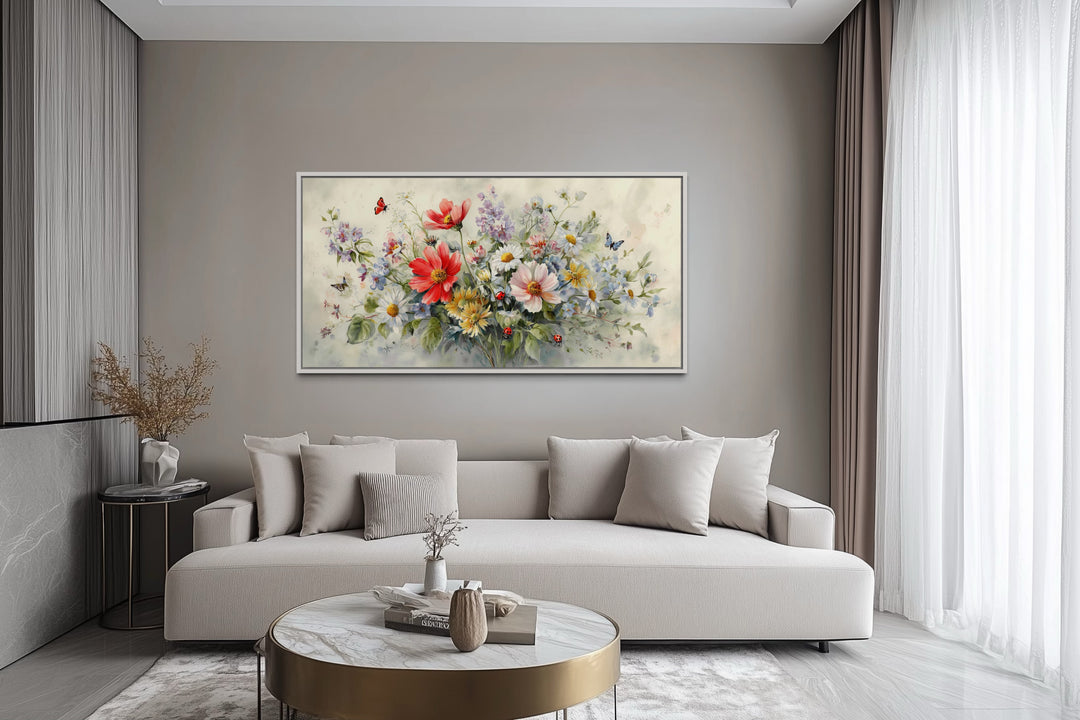Framed watercolor canvas of red wildflowers, butterflies, and ladybugs above a modern beige sofa.
