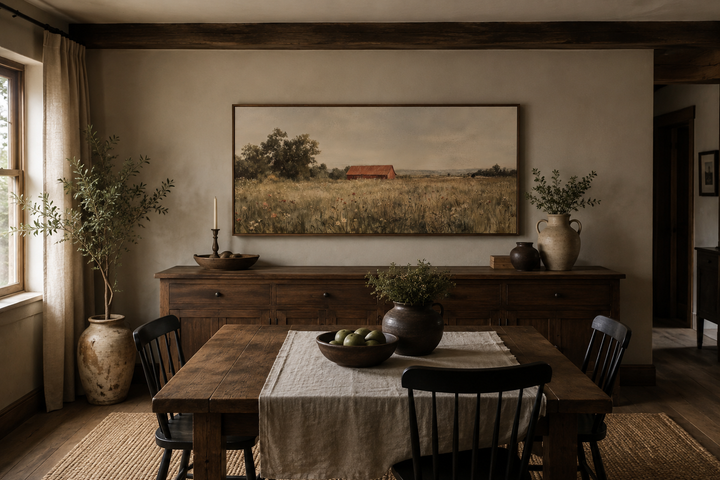 Horizontal canvas art of a red barn in a wildflower field above a wooden sideboard in a dining room.