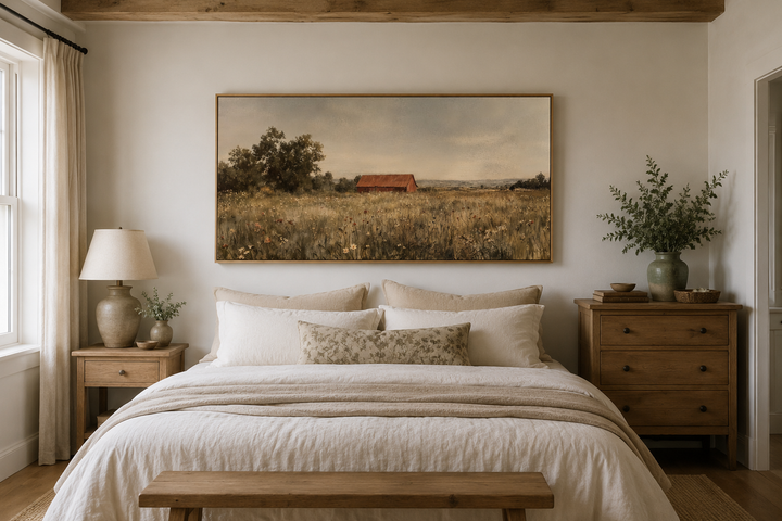 Red barn in a wildflower field canvas wall art hanging above a bed in a neutral farmhouse bedroom.
