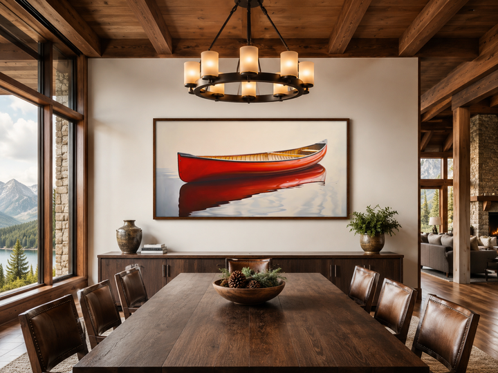 Framed canvas print of a red canoe on water, hanging in a rustic dining room with mountain views.