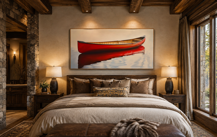 Framed canvas wall art of a red canoe on calm water hanging above a bed in a rustic cabin bedroom.