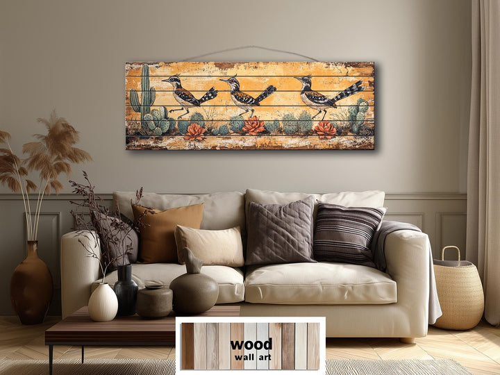 Horizontal wood wall art featuring three roadrunners in a desert scene above a neutral sofa.