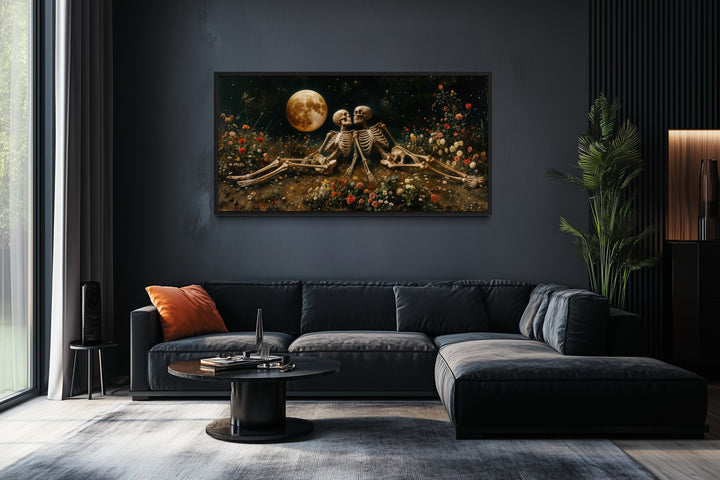 Gothic wall art of two skeletons in a flower meadow under a full moon above a black sectional sofa.