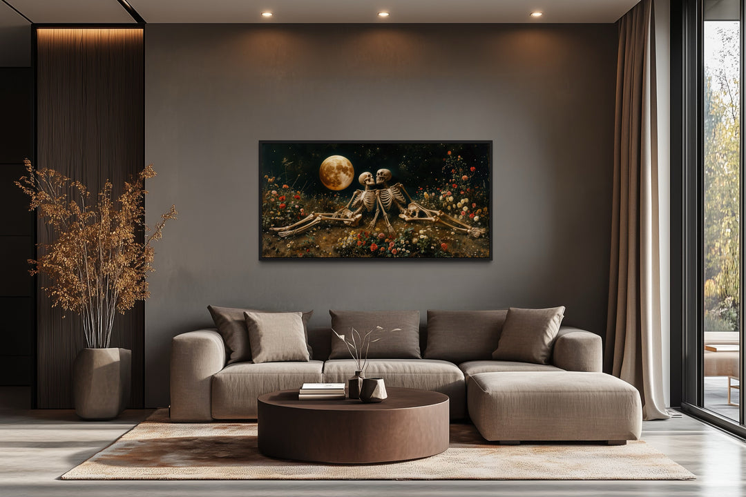 Romantic gothic wall art of two skeletons in a floral meadow under a full moon above a brown sofa.