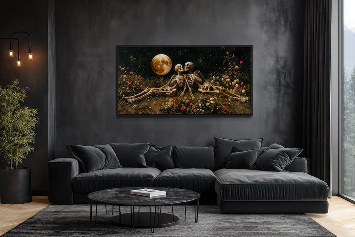 Gothic wall art of two skeletons in a flower meadow under a full moon above a black sofa.