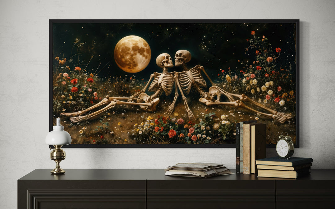 Framed gothic wall art of two skeletons in a flower meadow under a full moon above a dark dresser.