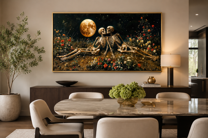 Framed gothic wall art of two skeletons in a floral meadow under a full moon above a dining table.