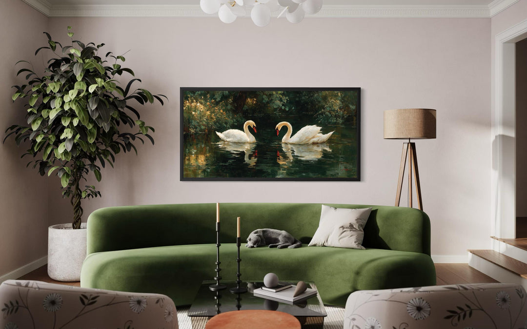 A framed canvas print of two white swans on a dark lake hangs above a green velvet sofa.
