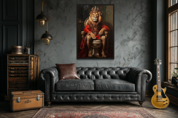 Framed canvas of a royal lion with a crown sitting on a toilet, hung above a black leather sofa.