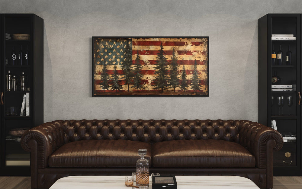 Framed canvas wall art of a rustic American flag with pine trees above a brown leather sofa.