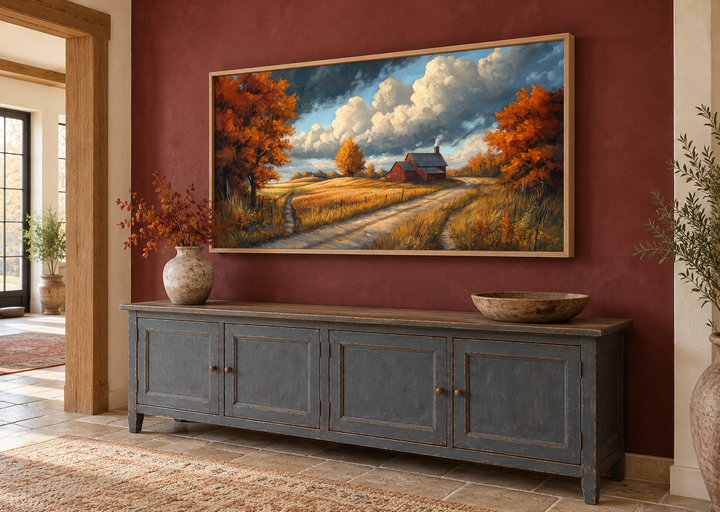 Rustic autumn barn landscape wall art in a light wood frame above a dark blue sideboard.
