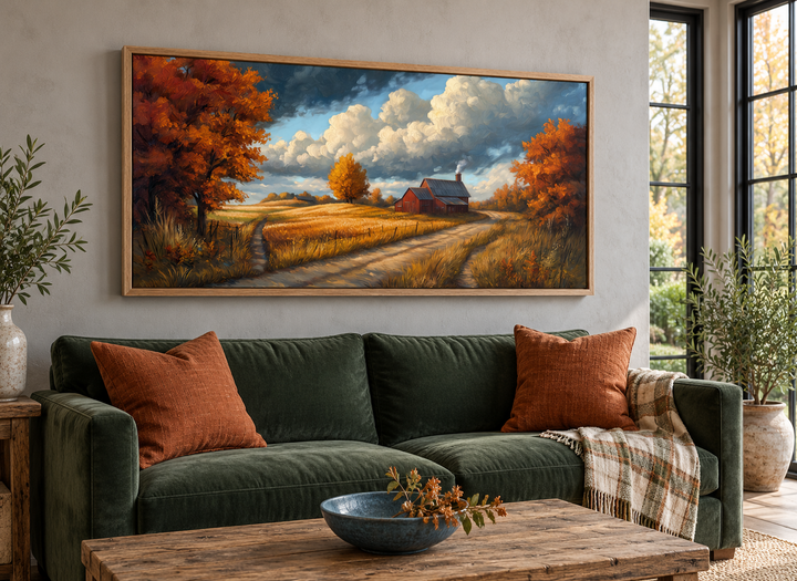 Rustic autumn barn landscape painting in a wood frame above a green sofa with orange pillows.