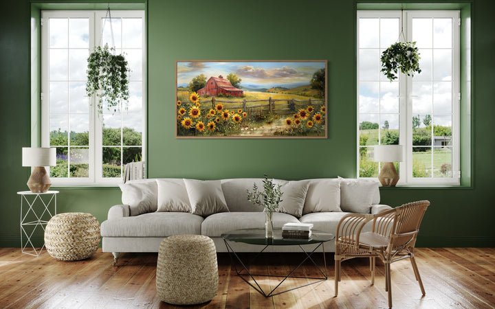 Panoramic canvas print of a rustic red barn and sunflowers displayed over a sofa in a green room.