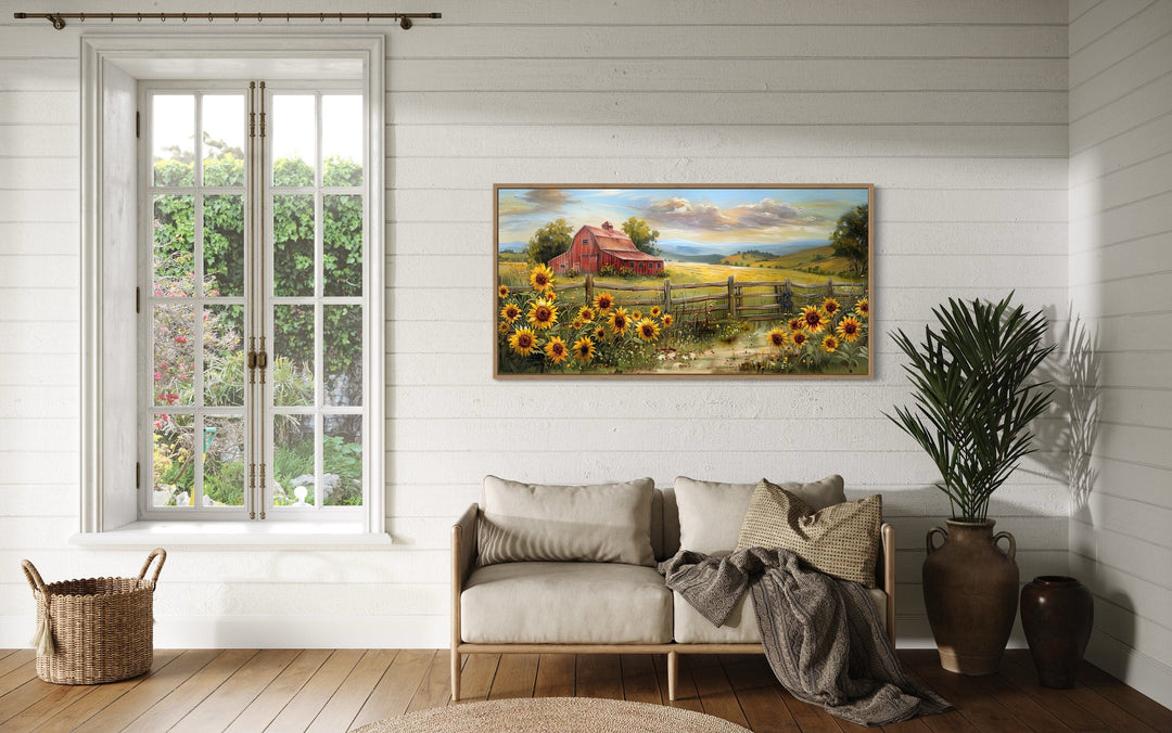 Rustic panoramic canvas print of a red barn and sunflowers hanging above a sofa in a farmhouse room.
