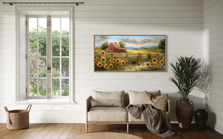 Rustic panoramic canvas print of a red barn and sunflowers hanging above a sofa in a farmhouse room.