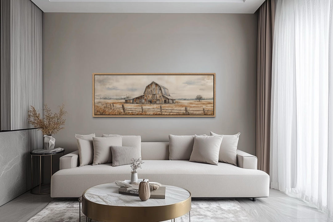 A long horizontal canvas print of a rustic barn hangs above a neutral sofa in a modern living room.