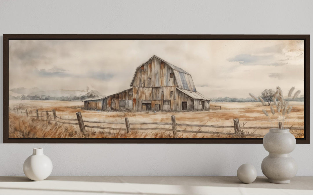 A long horizontal canvas print of a rustic barn in neutral tones, framed and hung on a white wall.