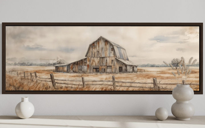 A long horizontal canvas print of a rustic barn in neutral tones, framed and hung on a white wall.