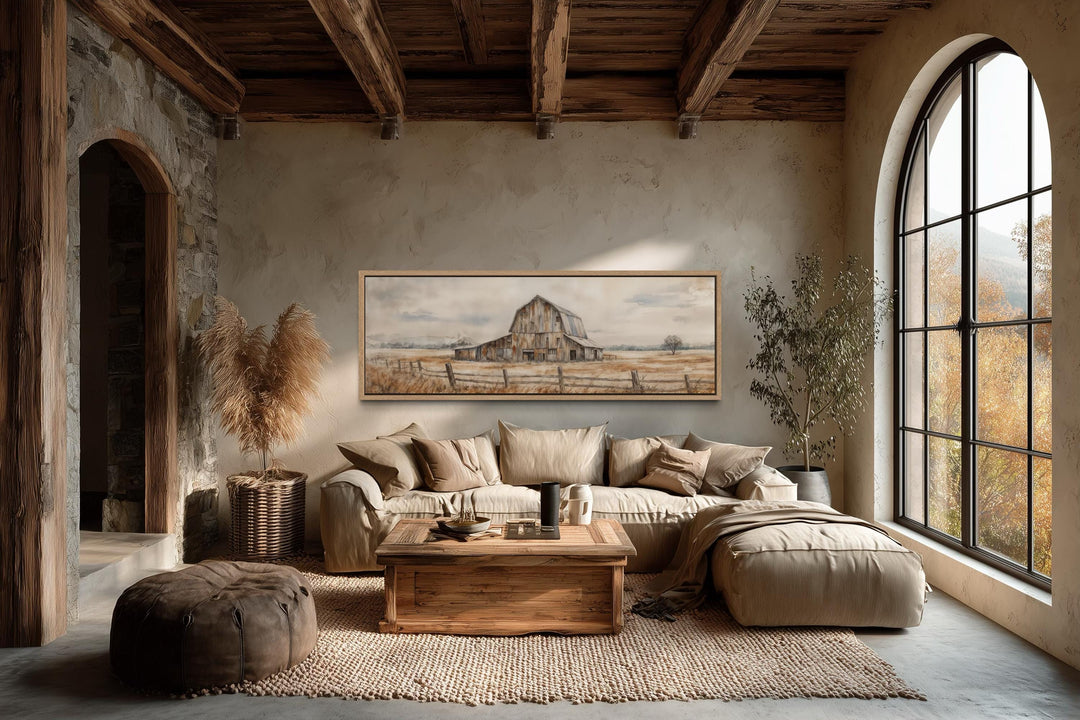 A long horizontal canvas print of a rustic barn hangs in a neutral, farmhouse-style living room.