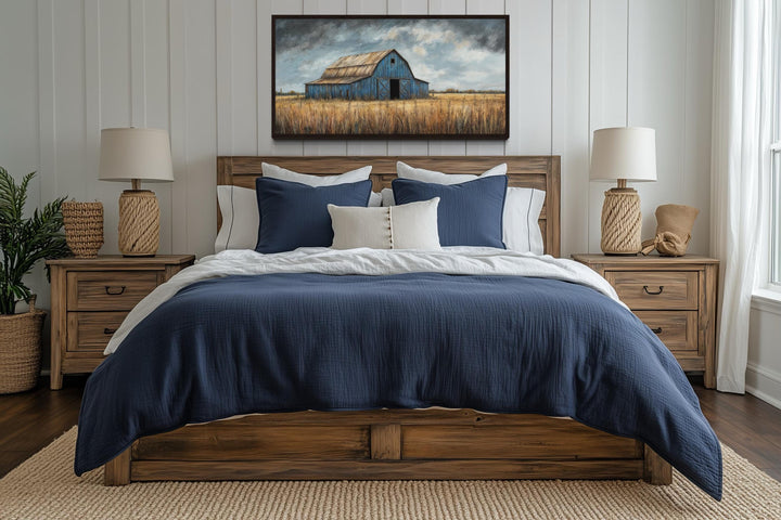 Rustic blue barn framed canvas wall art hanging above a bed in a farmhouse-style bedroom.