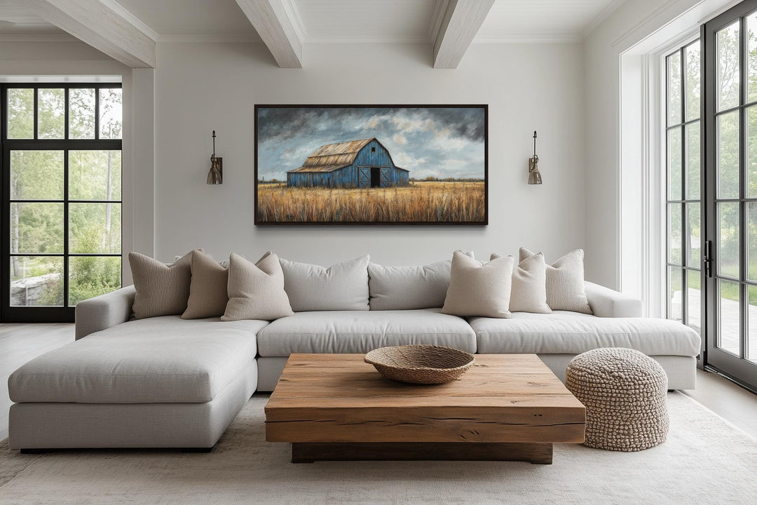 Rustic blue barn framed canvas wall art hanging above a neutral sectional sofa in a farmhouse room.