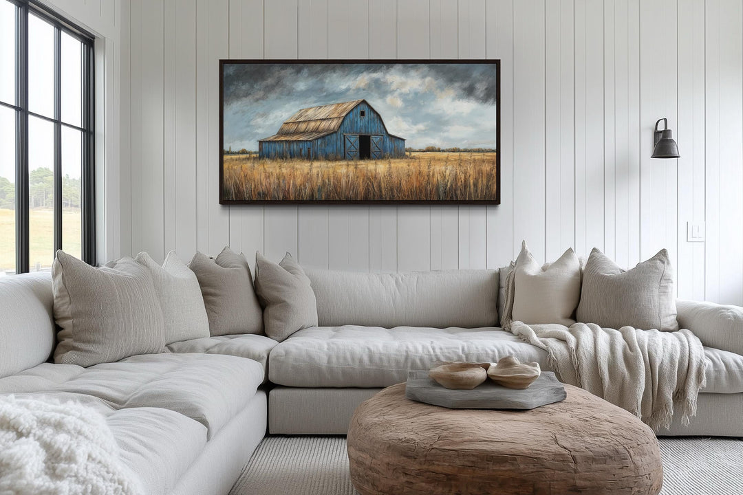 Rustic blue barn framed canvas wall art hanging above a large neutral sectional sofa.