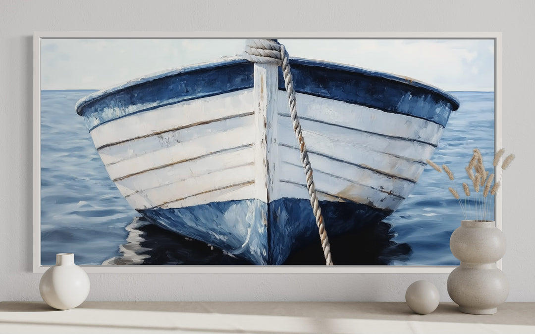 Rustic blue and white boat canvas wall art in a white frame above a shelf with decorative vases.