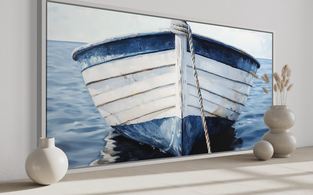 Rustic blue and white boat canvas wall art in a silver frame on a neutral shelf with decor.