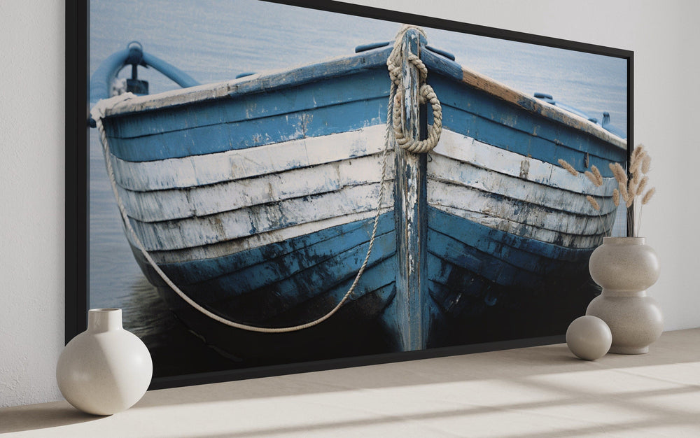 Rustic blue and white boat canvas print on a wall with decorative vases and pampas grass.
