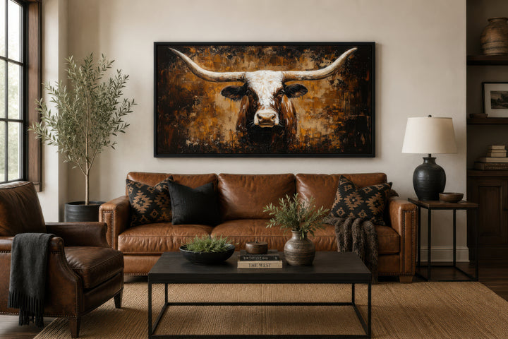 A large horizontal canvas painting of a longhorn bull hangs above a brown leather sofa.