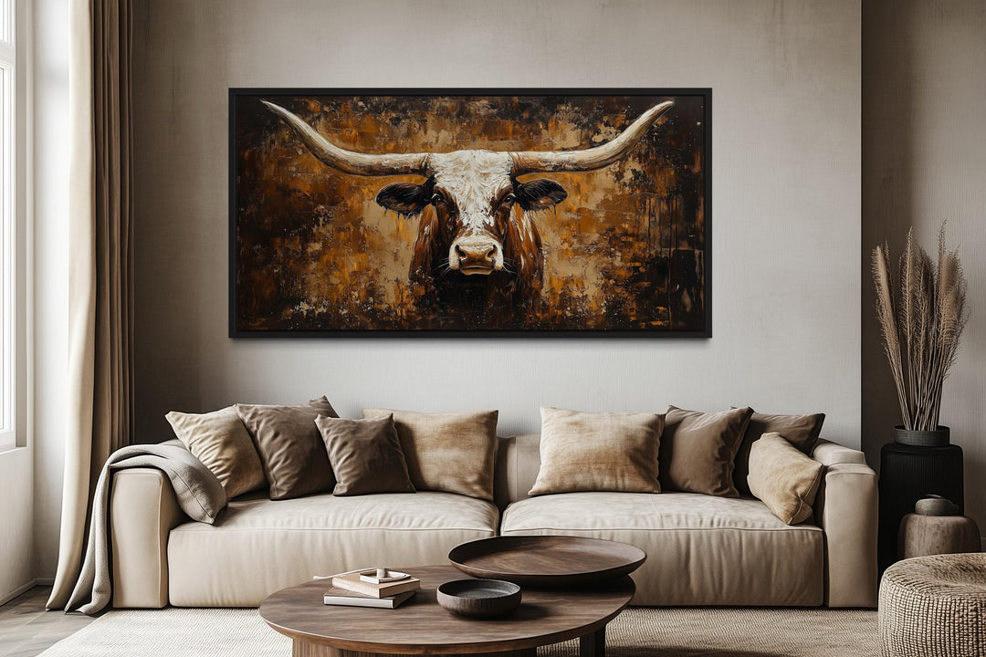 A rustic brown longhorn bull painting on a textured abstract background hangs above a beige sofa.