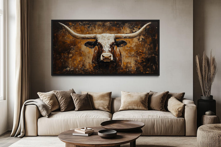 A rustic brown longhorn bull painting on a textured abstract background hangs above a beige sofa.