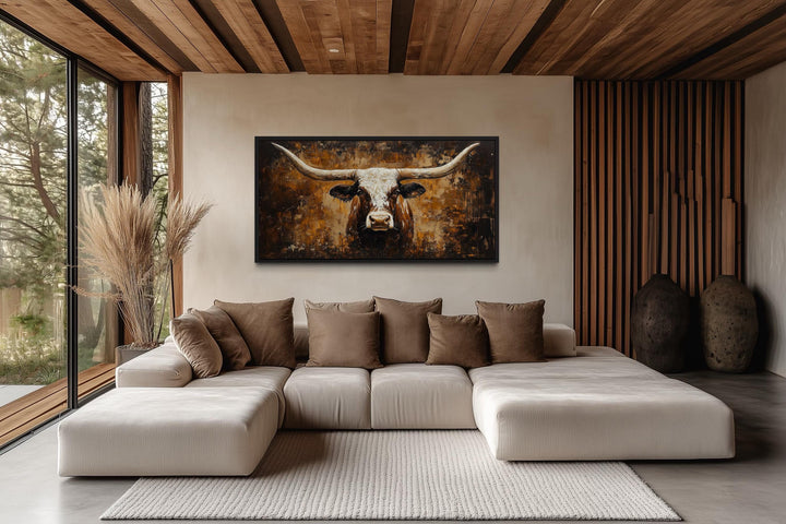 A rustic brown longhorn bull painting on a canvas wall art above a modern sectional sofa.