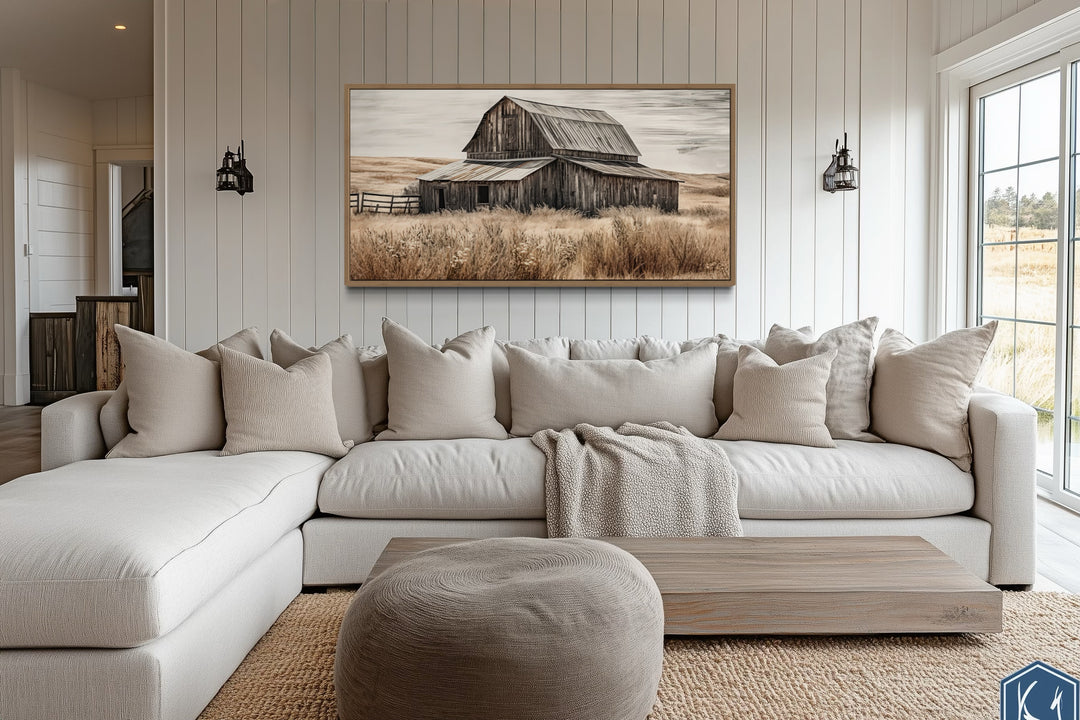 Rustic old farm barn painting on wood framed canvas wall art above a neutral sectional sofa.