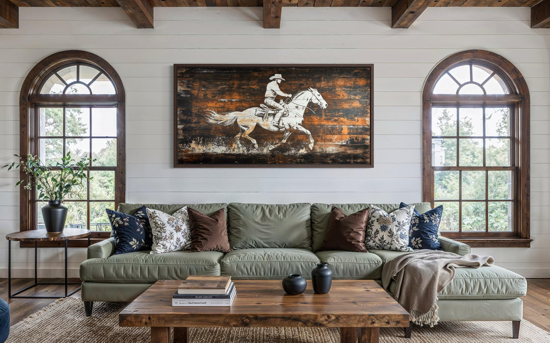 Rustic cowboy on horse on wood planks canvas wall art hanging above a green sofa in a rustic room.