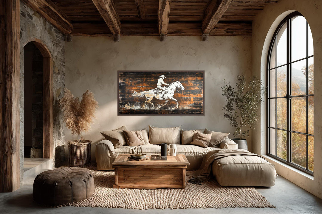 Rustic cowboy on horse canvas wall art on dark wood planks hanging in a modern rustic living room.