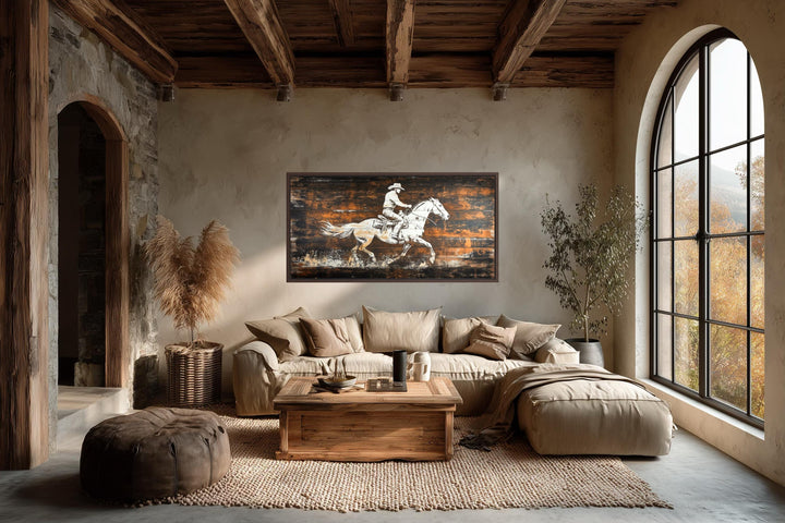 Rustic cowboy on horse canvas wall art on dark wood planks hanging in a modern rustic living room.